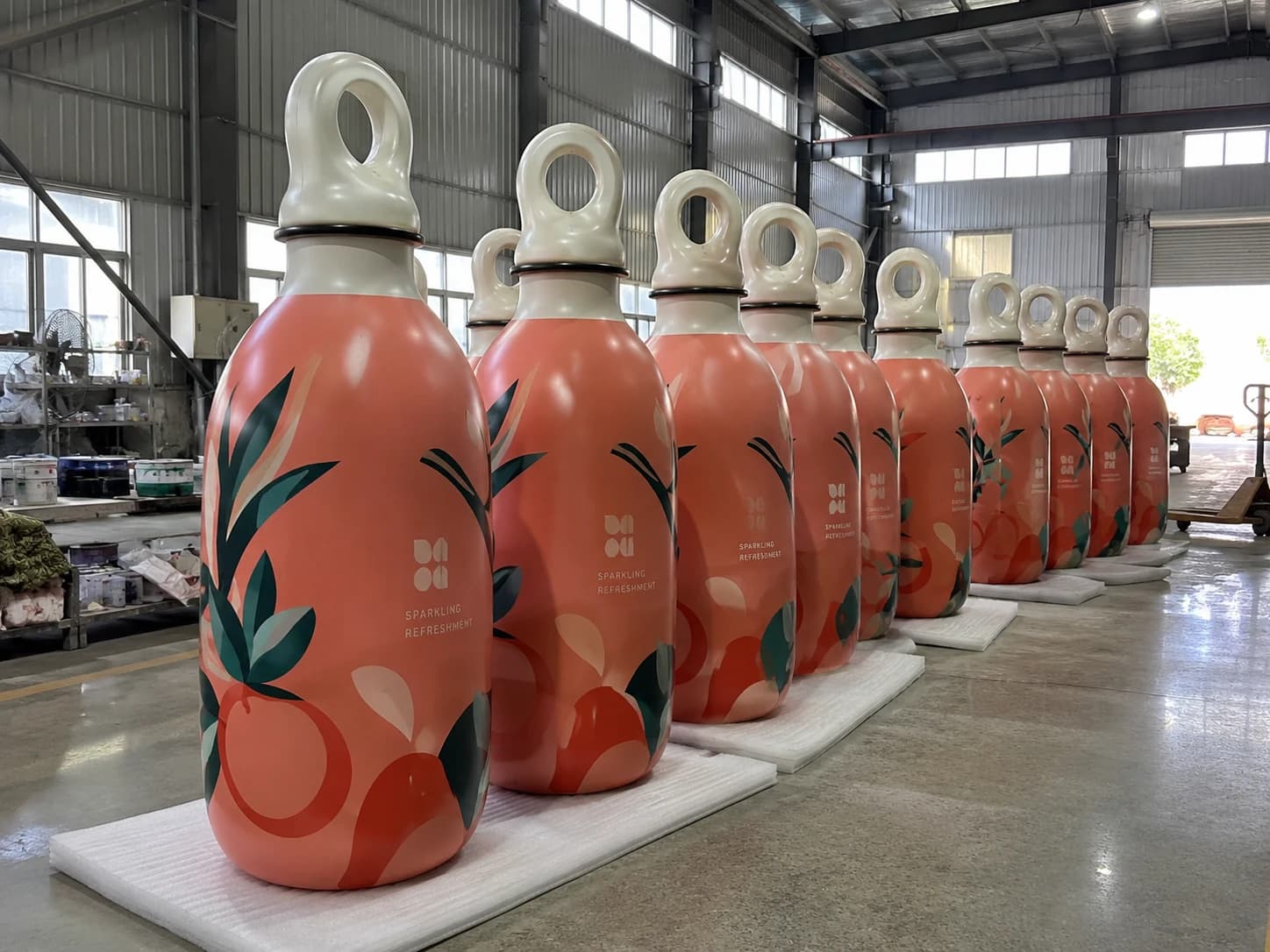 Multiple matching oversized beverage product replicas arranged in a production workshop