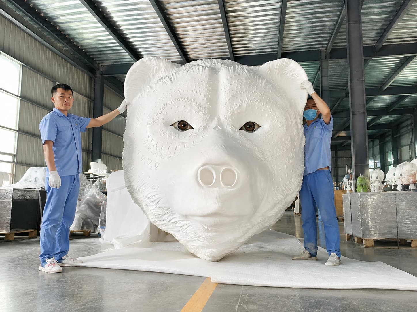 Large white bear sculpture shown at full scale with workers inside the fabrication workshop.