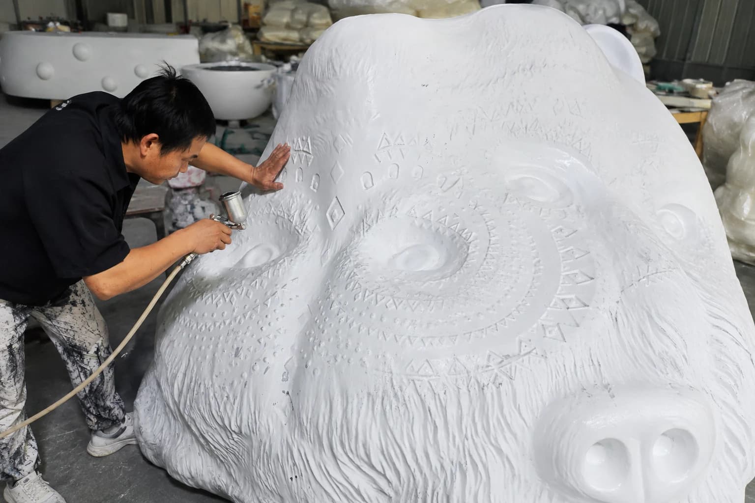 Worker applying surface treatment to detailed geometric and fur textures on a large bear sculpture.