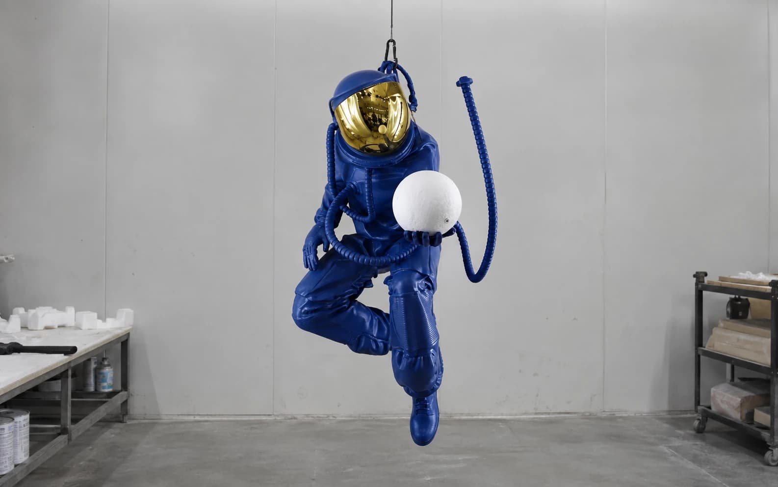 Front view of the finished suspended astronaut sculpture with mirrored visor, white sphere and visible hose arrangement.