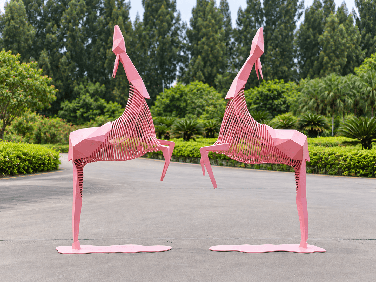 Pink geometric twin deer sculptures with bases in a landscaped garden