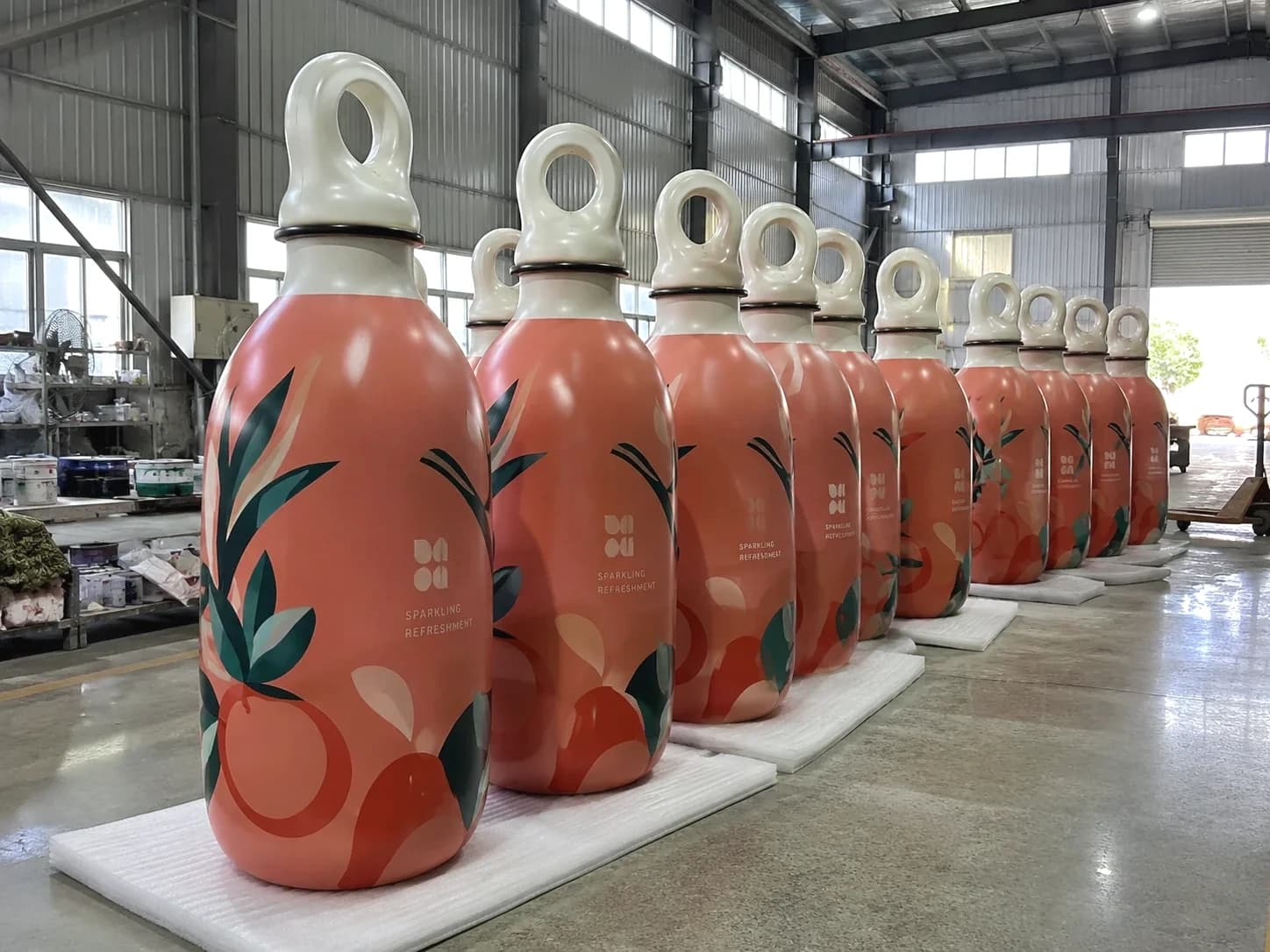 Multiple oversized beverage replicas arranged together in a production workshop